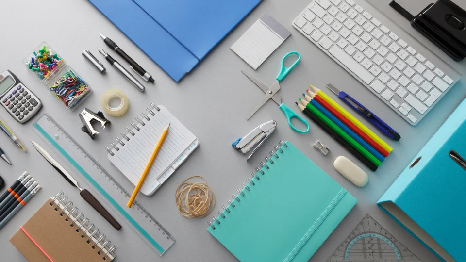 Notebooks, pens, a laptop, and other office supplies are laid out on a table, showcasing common business expenses