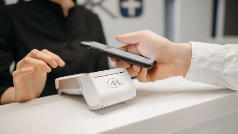 A customer uses a mobile phone to complete a transaction through a payment terminal, incurring payment processing fees