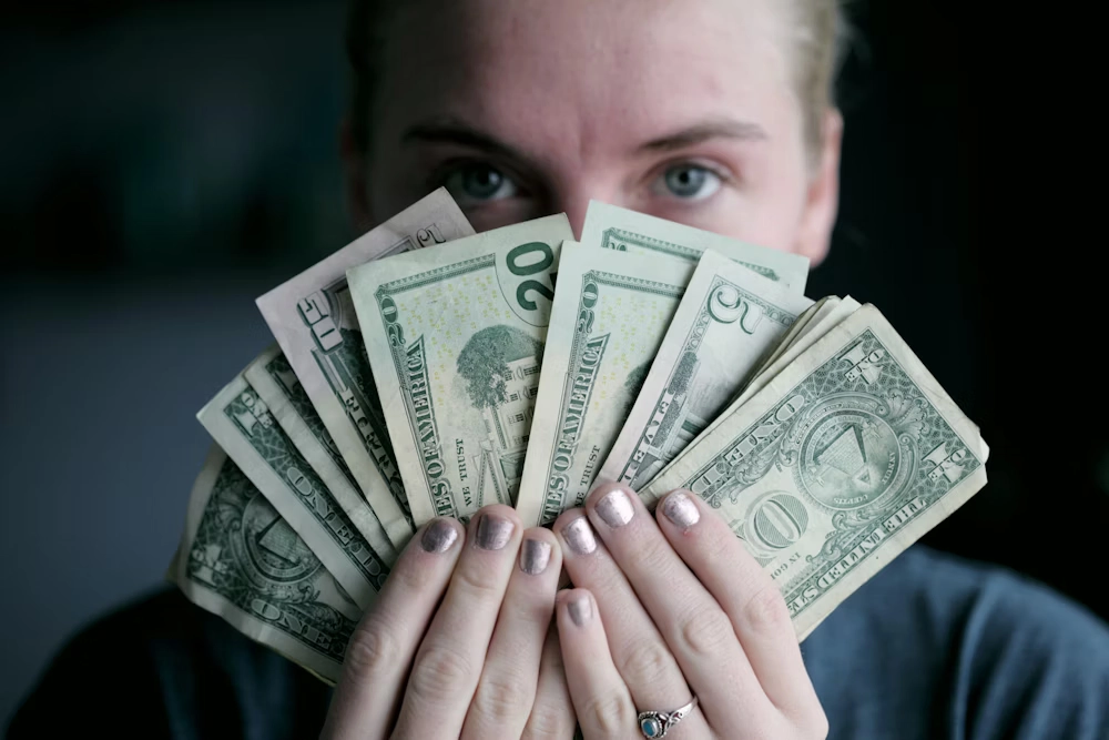 calculator, laptop, and stacks of cash on a wooden desk