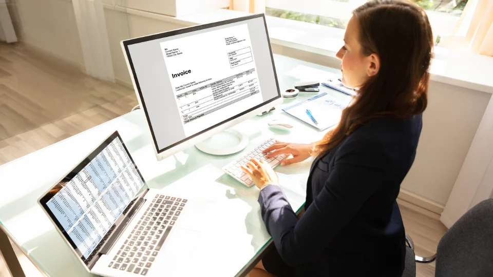 An outsourced payroll specialist works on invoices for a company's payroll process using a computer