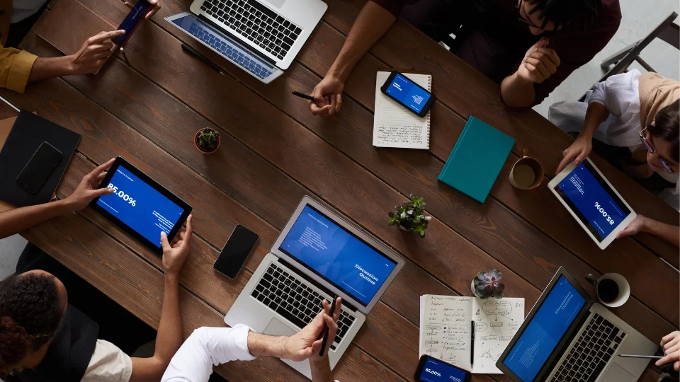 Business professionals sit around a table with laptops, discussing payroll outsourcing options for their company