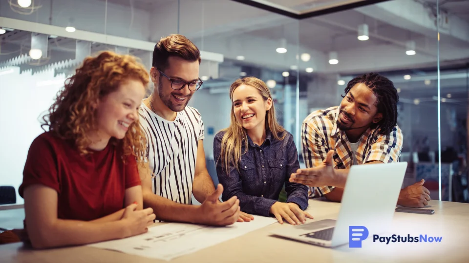 A cheerful team of employees gathered around a desk, smiling and looking at a laptop together