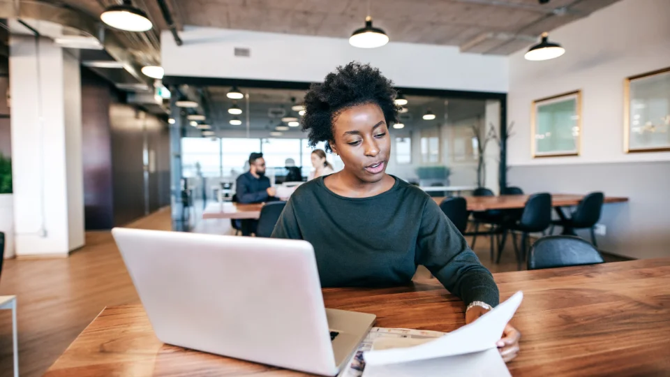 A woman sitting at a table with a laptop looking at documents